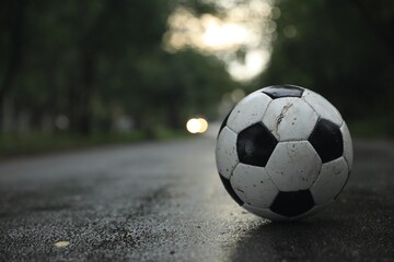 Fototapeta na wymiar Dirty leather soccer ball on wet road, space for text