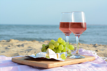 Glasses with rose wine and snacks on sandy seashore. Space for text