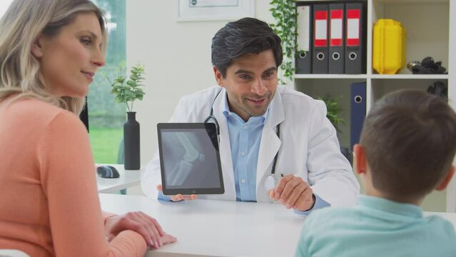 Doctor or GP in white coat meeting mother and son for appointment looking at scan on digital tablet as doctor gives boy high five - shot in slow motion