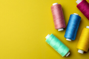Different colorful sewing threads on yellow background, flat lay. Space for text