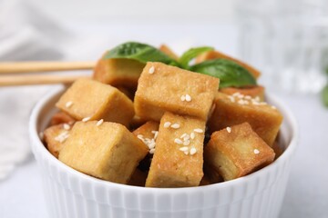 Bowl with delicious fried tofu, basil and sesame seeds on table, closeup