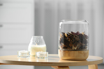 Decorative jar with aromatic potpourri and candles on wooden table in room, space for text