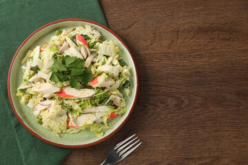 Delicious salad with Chinese cabbage, crab sticks and parsley on wooden table, top view. Space for text