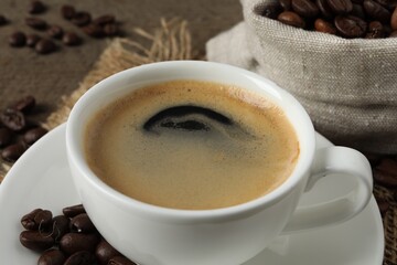 Cup of aromatic coffee and beans on wooden table, closeup