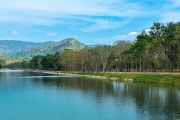 Beautiful and peaceful view of large reservoir with surrounding mountain and trees in beautiful sunshine and cloudy sky in Thailand. Tranquil and beautiful natural scenery landscape of reservoir lake.