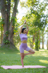 Obraz na płótnie Canvas Yoga in the park Beautiful Asian woman practicing yoga poses in the park with beautiful and balanced postures.