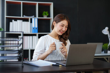 Beautiful young Asian businesswoman using laptop enjoy working, taking notes, reviewing assignments and enjoy working.
