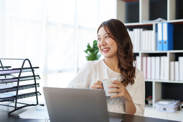 Beautiful young Asian businesswoman using laptop enjoy working, taking notes, reviewing assignments and enjoy working.