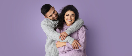 Happy young couple in warm sweaters on lilac background