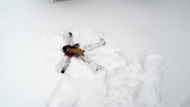 A man wearing a red jacket making snow angels at the snowy mountains of Banff Canada