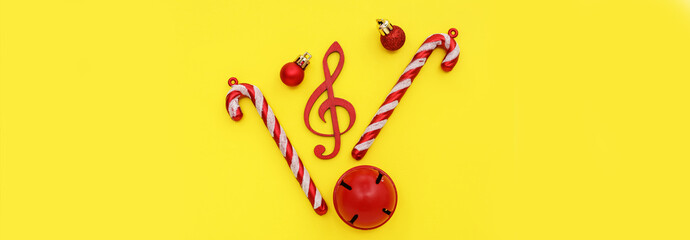 Violin clef with Christmas balls, jingle bell and candy canes on yellow background