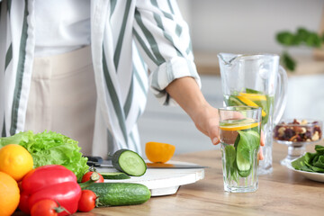 Young woman drinking infused water in kitchen, closeup