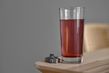 Glass of water with soluble tablets on table near grey wall