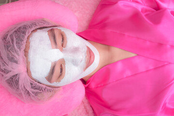 A pampered customer lays on a bed with waiting for the collagen mask to be absorbed into the skin. At an Aesthetic center or dermatology clinic.