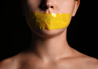 Young woman with taped mouth on dark background, closeup. Censorship concept