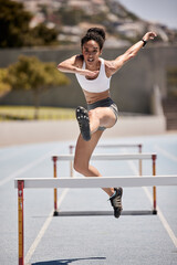 Fitness, hurdles and athlete jumping on track at an outdoor stadium for cardio workout. Sports,...