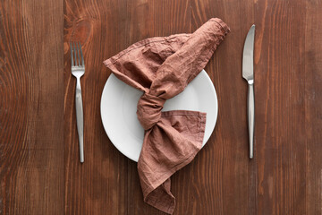 Simple table setting with napkin in plate and cutlery on wooden background