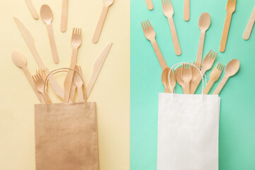 Paper bags with wooden cutlery on green and yellow background