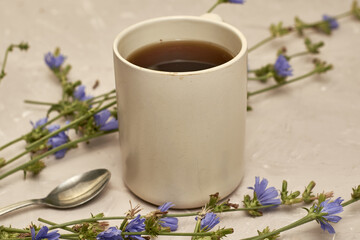 chicory drink in a coffee mug and a spoon next to chicory flowers