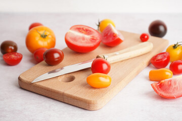 Wooden board of fresh tomatoes and knife on light background, closeup