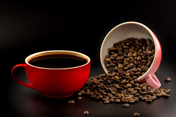 Coffee in red cup and coffee beans spilled from pink cup on blacd background.