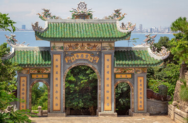 Fototapeta na wymiar Traditional colorful Asian gate structure and tropical forest coastline in Chùa Linh Ứng Buddhist temple in DaNang Vietnam 