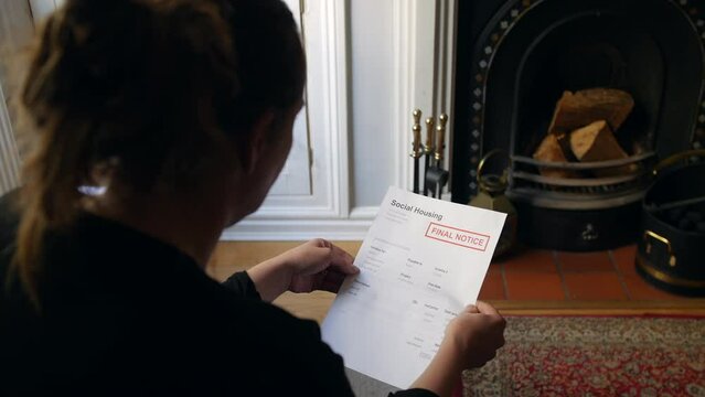 An unrecognizable female opening a debt letter. The woman is reading a social housing bill final notice at home