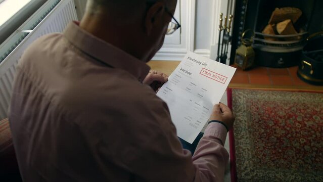 A lonely senior man opening a debt letter. The mature male is reading an electricity bill final notice at home