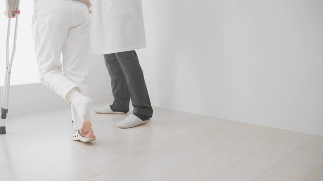 医者に介助されながら松葉杖をついて歩くミドル女性　リハビリイメージ