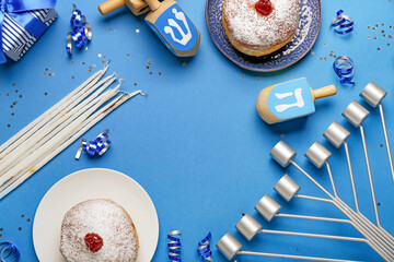 Frame made of plates with donuts, menorah, candles and dreidels for Hanukkah celebration on blue...