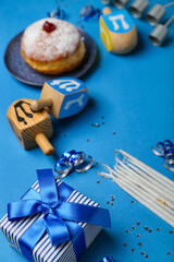 Gift with candles and dreidels for Hanukkah celebration on blue background, closeup