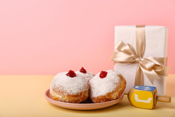 Plate with tasty donuts, dreidel and gift for Hannukah celebration on color background
