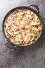 Champignon mushrooms in a creamy wine sauce with bacon and parmesan close-up in a frying pan on the table. Vertical top view from above