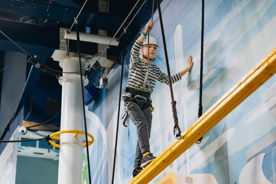 Caucasian Boy Climbing In Adventure Park Passing Obstacle Course. High Rope Park Indoors