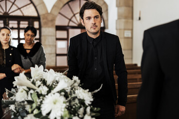 Funeral, death and grief with a man pallbearer carrying a coffin in a church during a ceremony. Flowers, suit and loss with a male holding a casket while walking through a chapel for mourning - obrazy, fototapety, plakaty