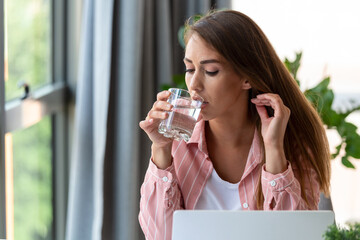 Headache. Close-up photo of a young woman, who is sitting in the office, getting hydrated, drinking water.