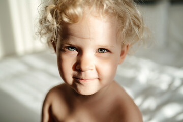 Close-up portrait of a small child with a bright look, curly hair and an expectation emotion.