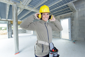 female builder putting on her earmuffs - obrazy, fototapety, plakaty