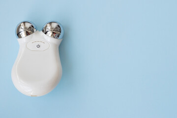 Microcurrent toning device for facial massage on blue. The concept of wellness, beauty and skin care. flat plan