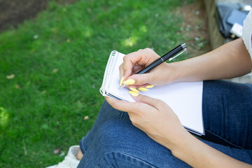Woman with pen writing on notepad in the outdoors.