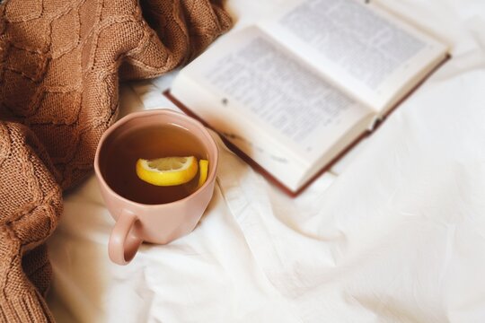 Winter aesthetics flat lay photography. Brown wool sweater, pen book and cup of tea with lemon. Breakfast on a bed