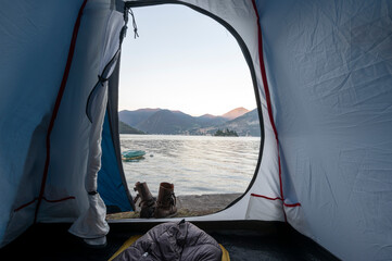 Aube à travers l'ouverture d'une tente de camping sur un paysage de lac entouré de montagnes à...