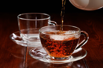 Black tea is poured into a glass cup from a teapot. Selective focus.