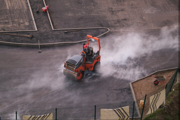 Orange asphalt paver machine laying asphalt road in the rainy day and steam rising from the asphalt, top view	
