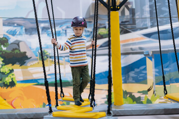 caucasian boy climbing in adventure park passing obstacle course. high rope park indoors