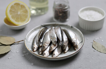 Fresh sardines in a plate and ingredients for salting fish: salt, oil, lemon and spices on the table. Selective focus. Traditional Spanish cuisine