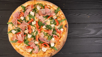 Pizza with prosciutto ham arugula and parmesan on dark wooden background top view. Italian cuisine. Banner.