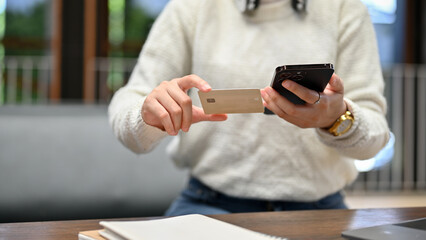 A young woman holding a credit card and smartphone, using mobile banking or internet banking