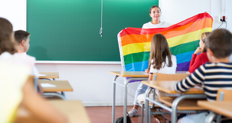 Teacher explaining meaning of LGBT flag to kids in classroom during lesson in school.