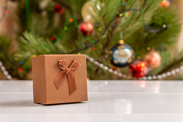 Gift box with bow and blurred Christmas tree with twinkling party lights and toy balls.